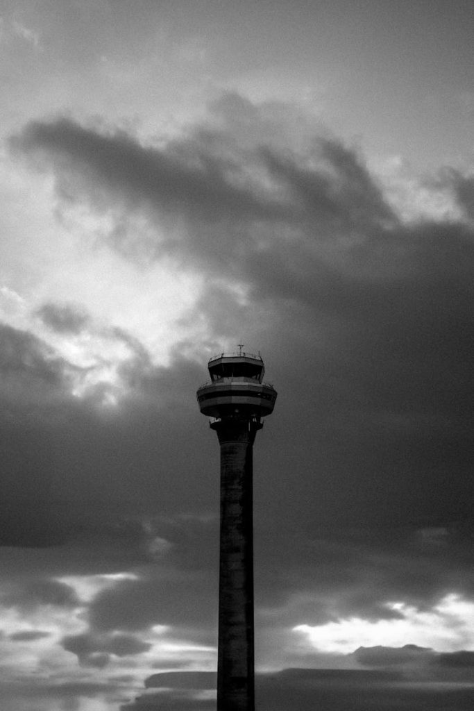 Black and white photo of a control tower against a dramatic cloudy sky.